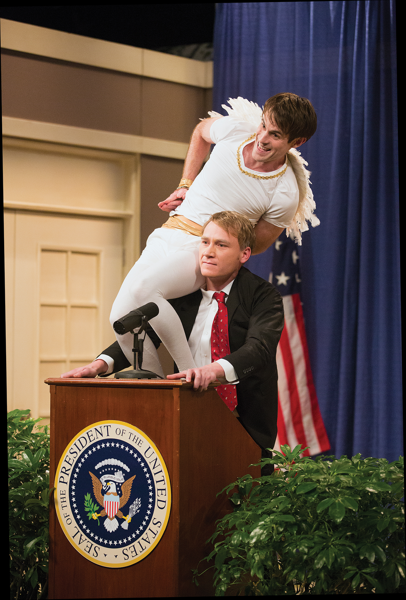 A cast member dressed as an angel sits on the shoulder of another cast member dressed as the president of the US.