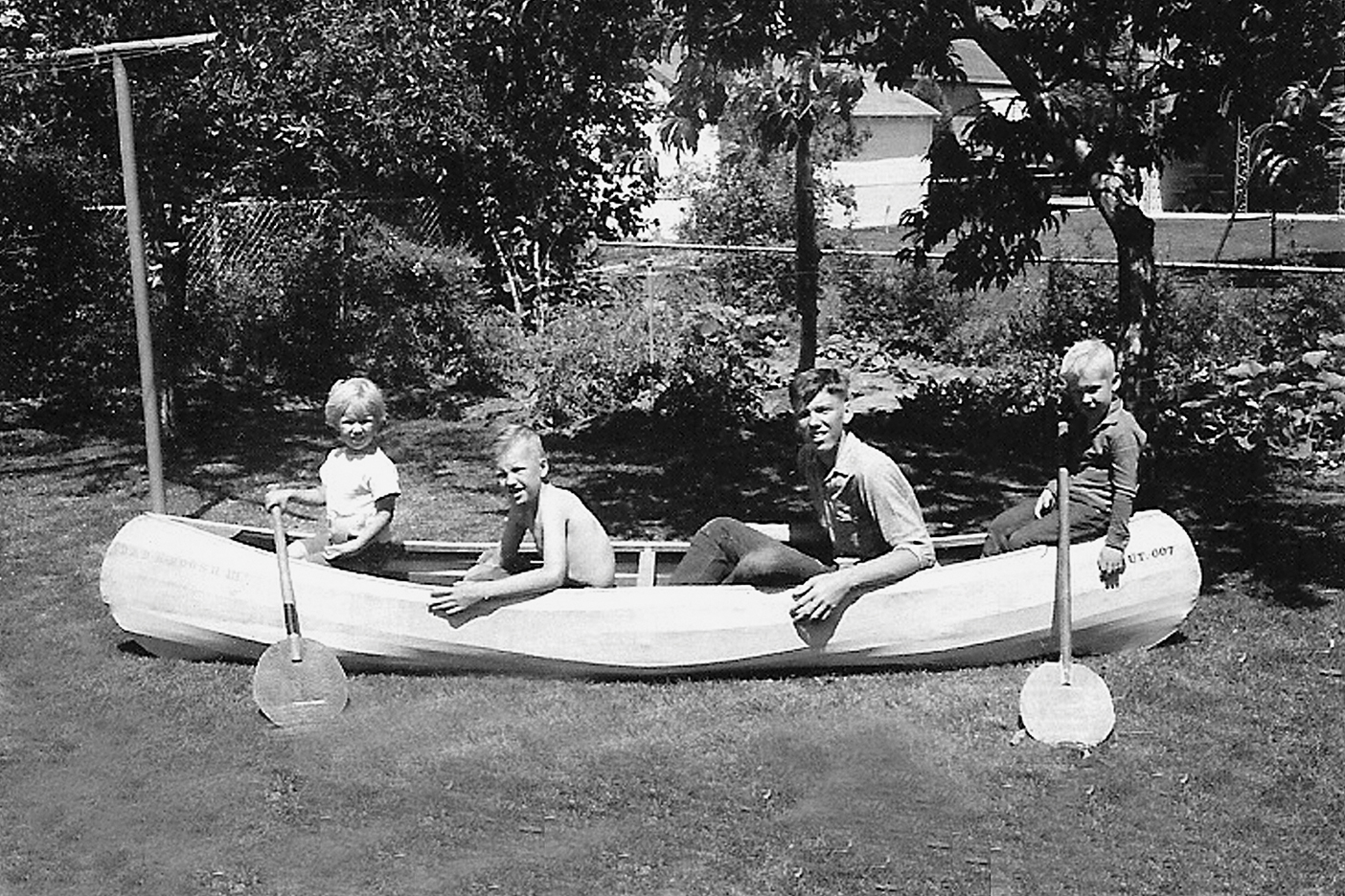 a black-and-white image of 4 boys, including Christensen sitting in a canoe in the backyard