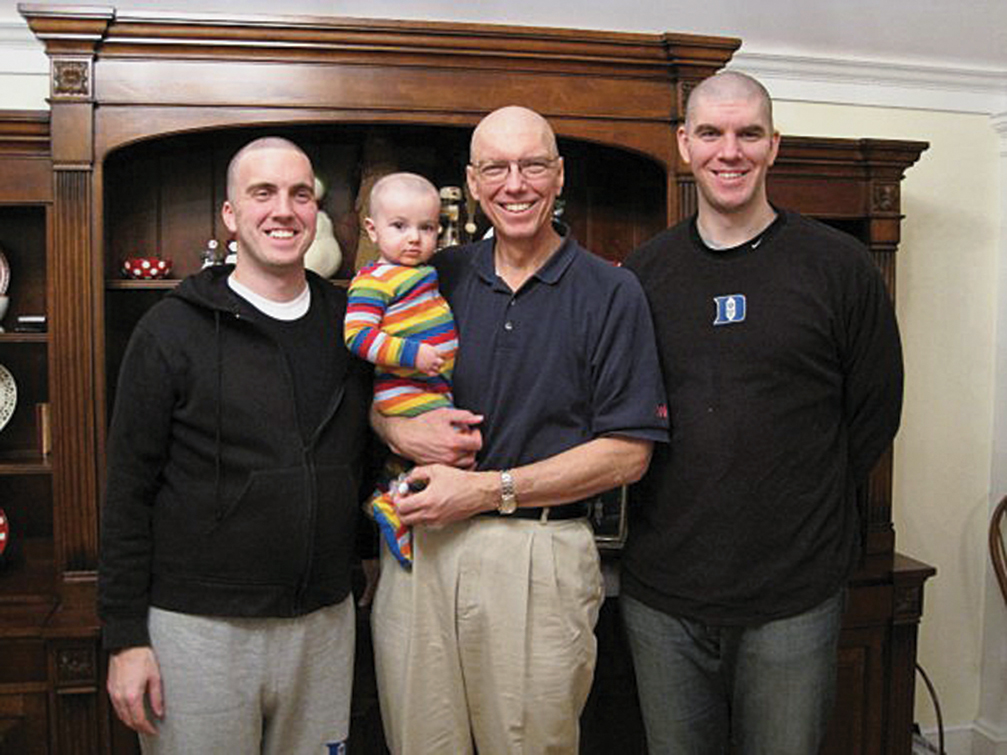 Christensen posing with his two sons and holding a toddler grandson in his arms