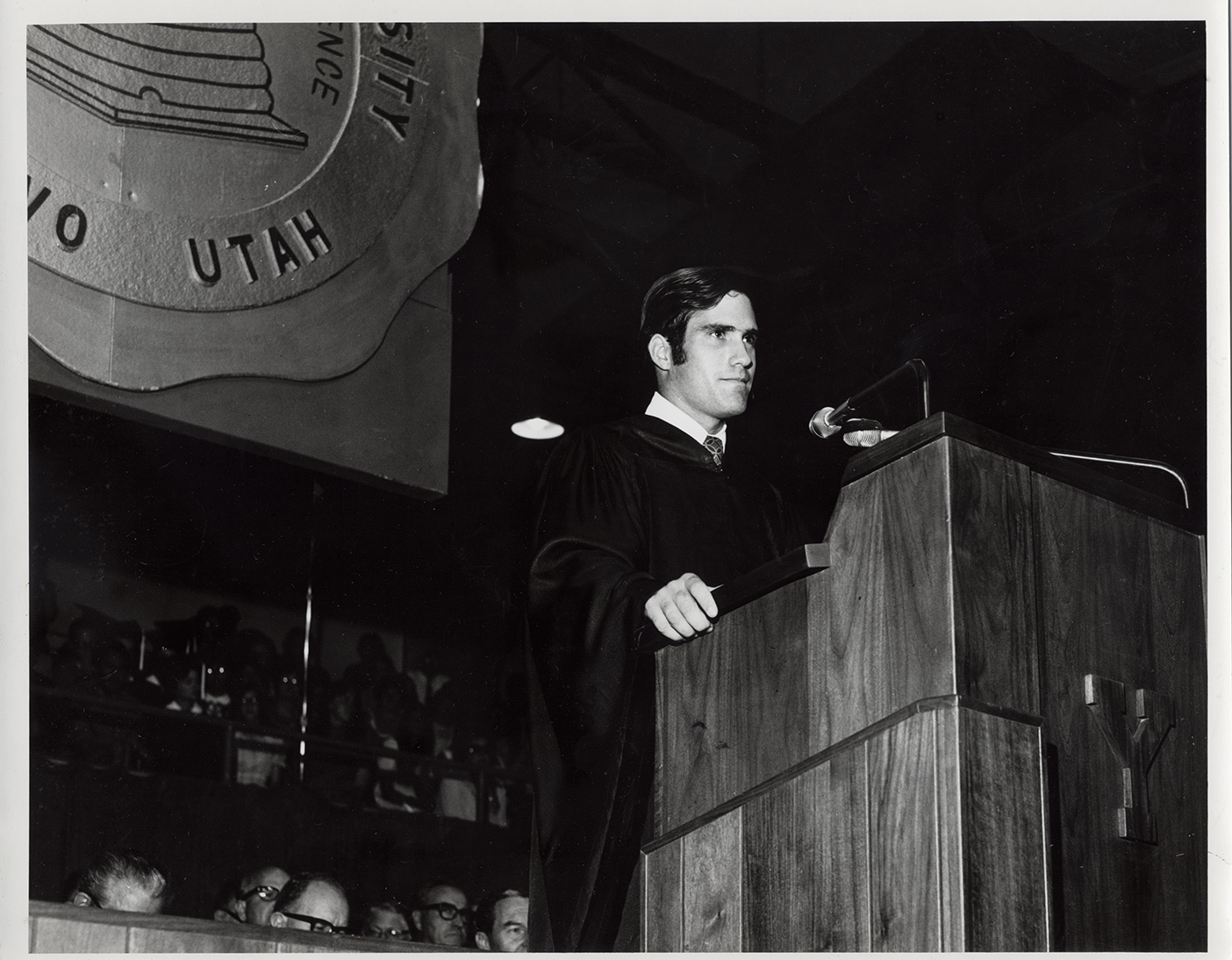 Romney stands at a podium in graduation robes.