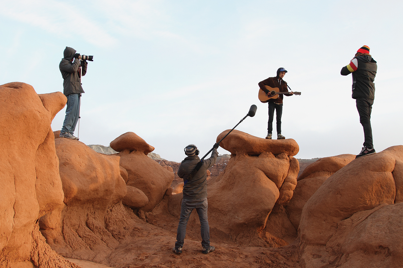 crew members film and hold mikes as a guitar player stands on a rock performing
