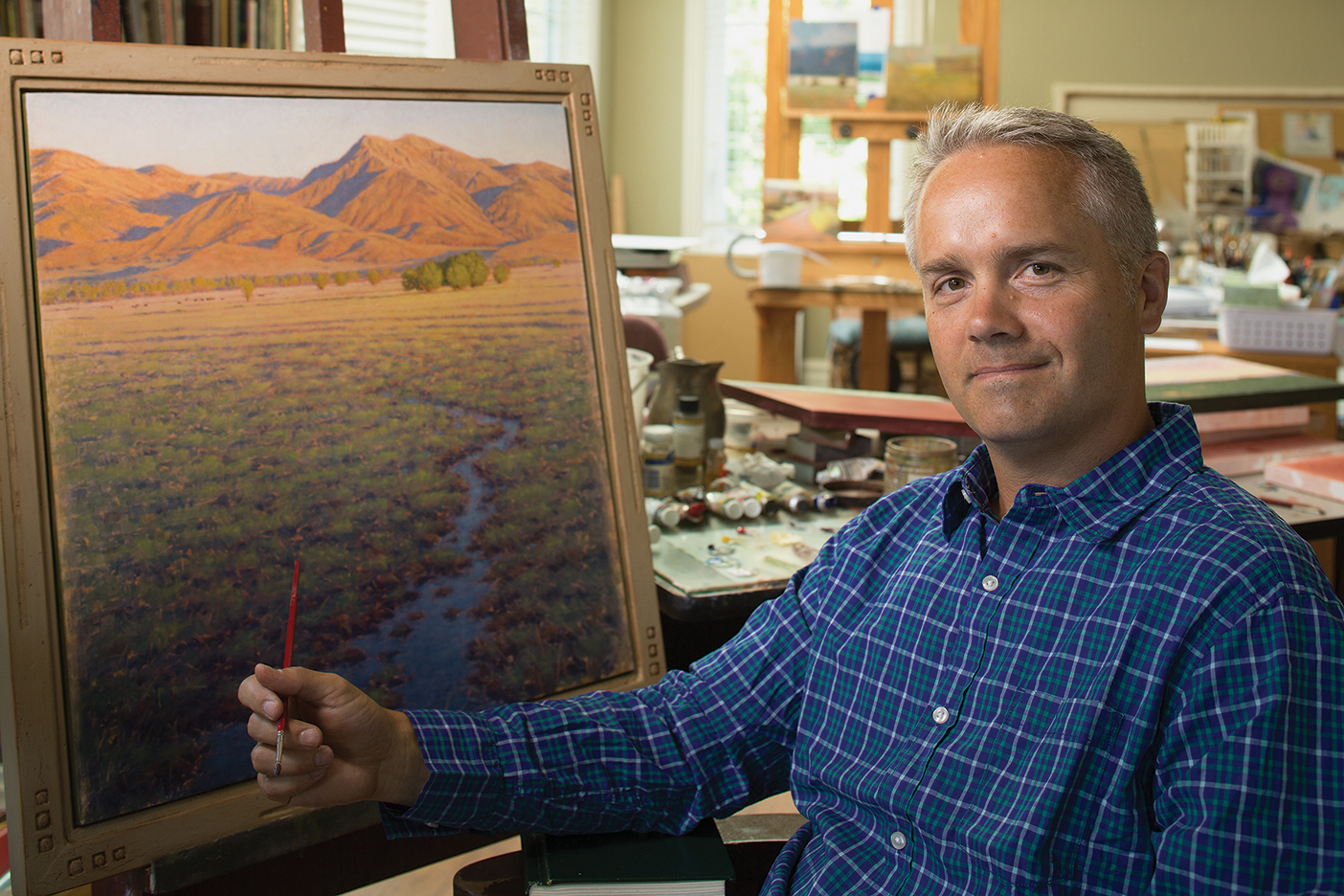 Kerry Soper sitting next to a landscape painting