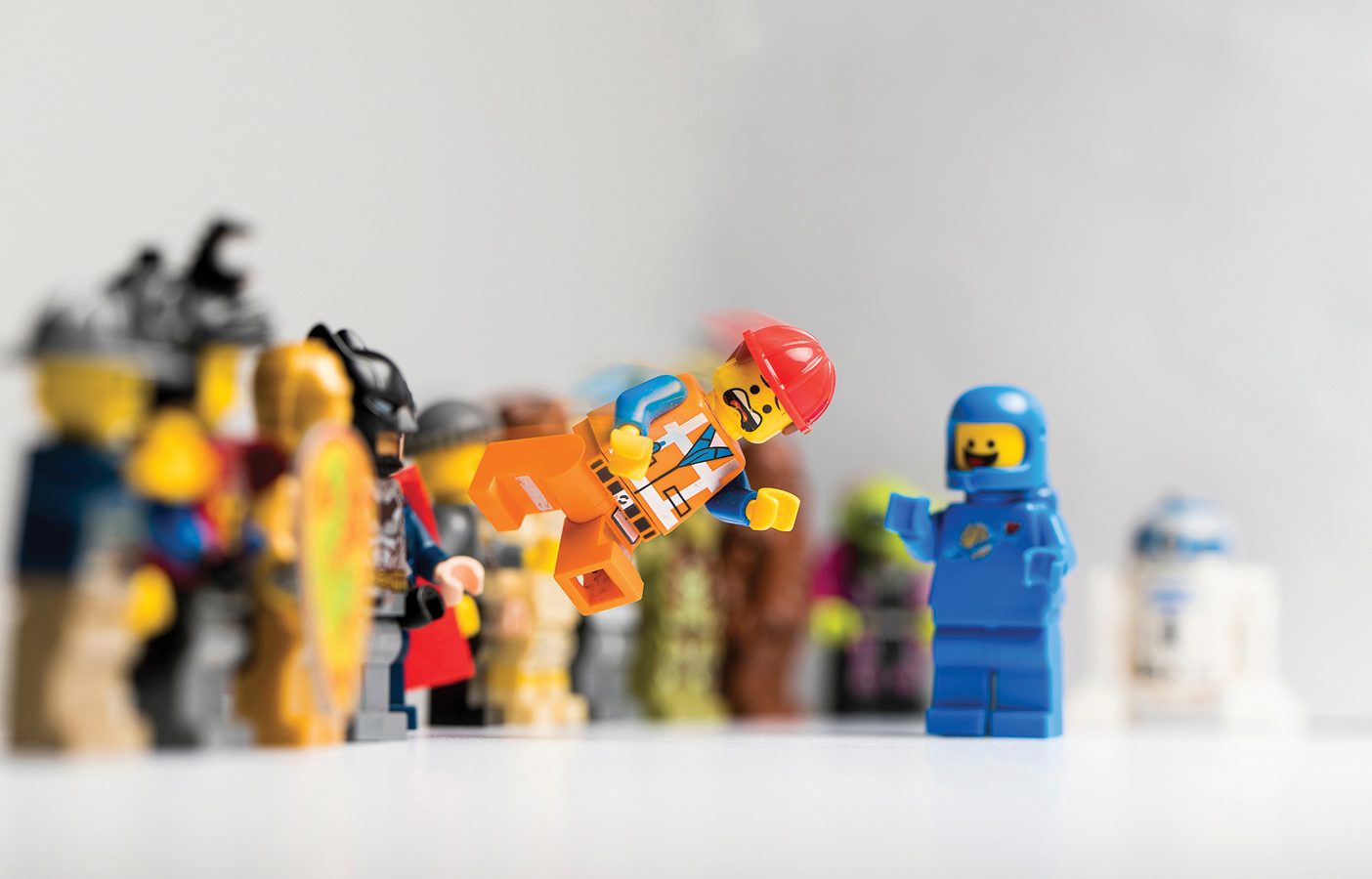 Lego figures stand at attention and watch as one figure flies through the air with a surprised look on its face.