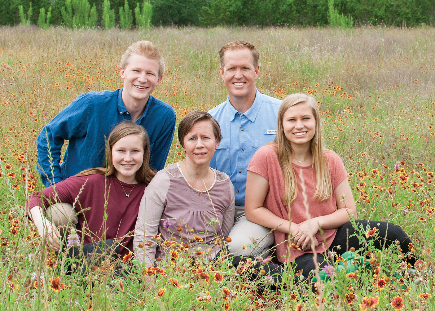 A family of five sits in a field of long grass.