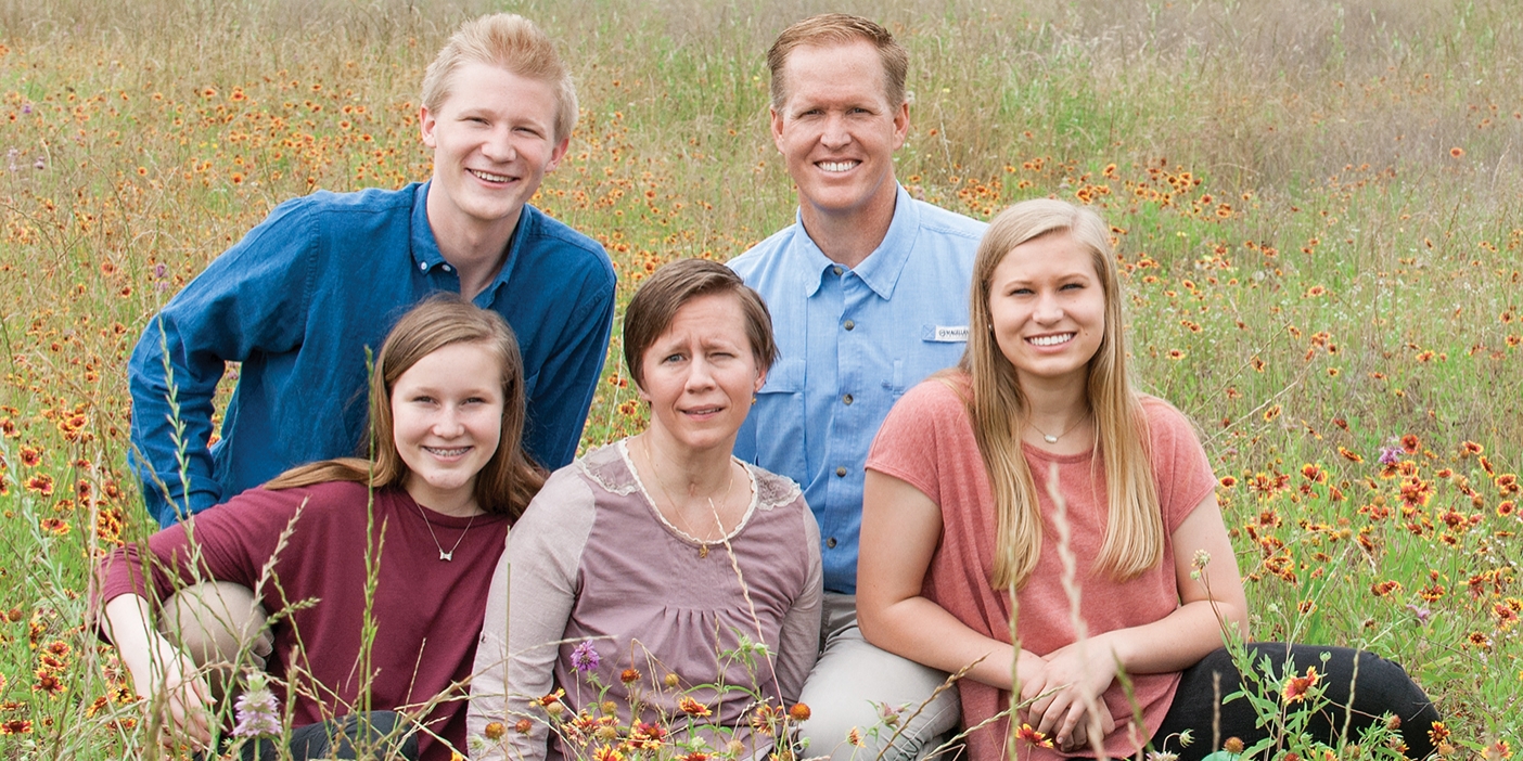 A family of five sits in a field of long grass.