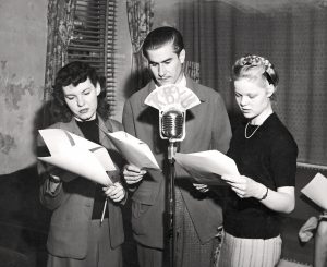 Three students gather around a microphone, performing a dramatic reading in a 1946 radio workshop at BYU. Photo from BYU Special Collections.