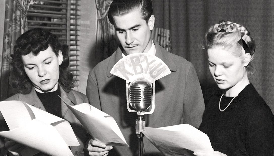 Three students gather around a microphone, performing a dramatic reading in a 1946 radio workshop at BYU. Photo from BYU Special Collections.