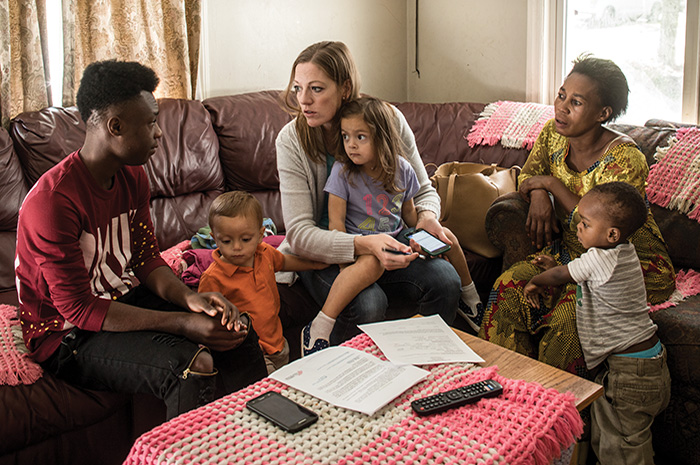 Deborah Worsham Valenzuela meets with a refugee family from the Democratic Republic of Congo. They all sit together on a sectional couch in the refugees' home.