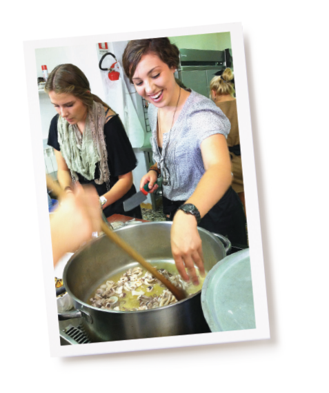 Two BYU students add chopped mushrooms to a large pot sizzling on the stove.
