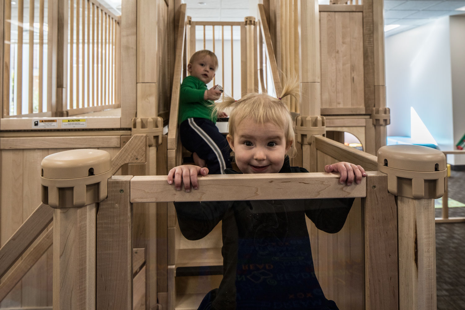 A tot with pigtails looks over the play structure railing and smiles at the camera in the new BYU family study room