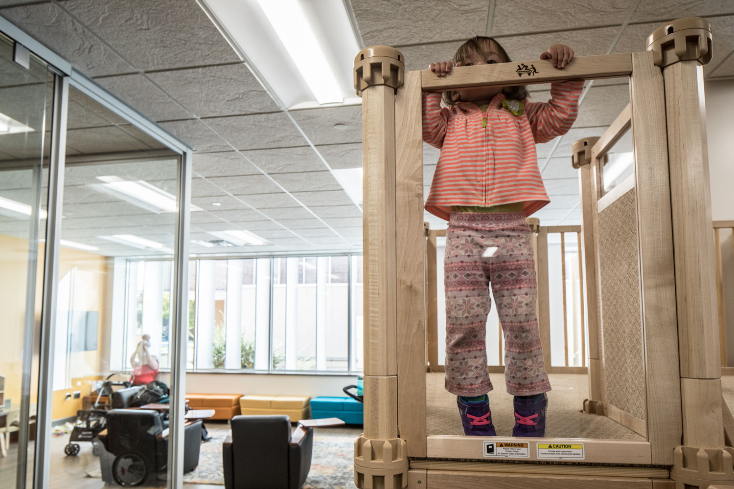 A child peeks over the railing of the play structure in the new family study room