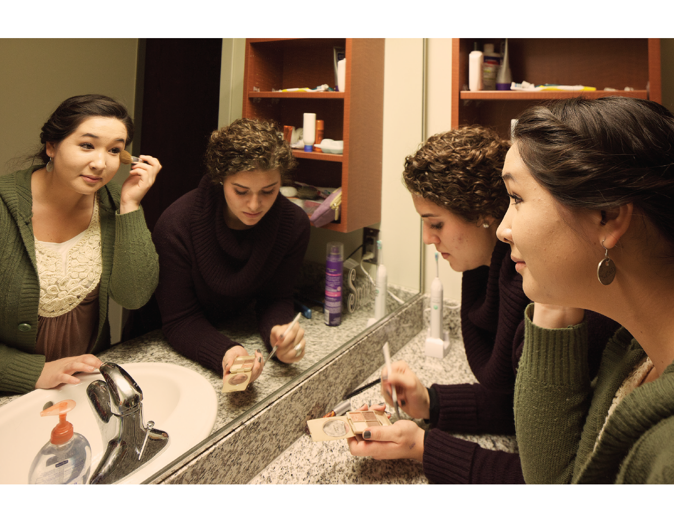 Two young woman get ready in front of a mirror.