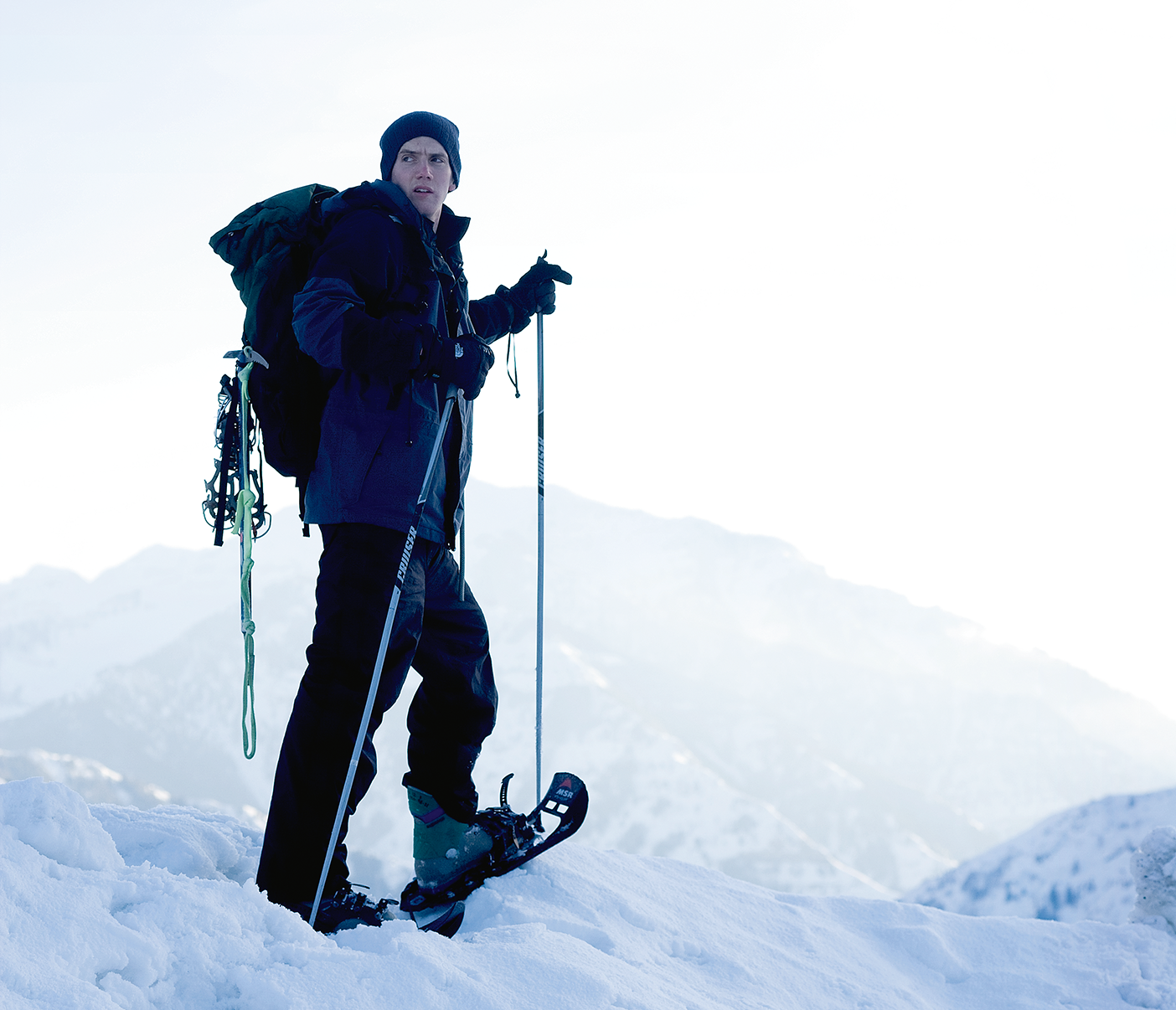 A photo of a man snowshoeing. He looks backward, over his right shoulder.