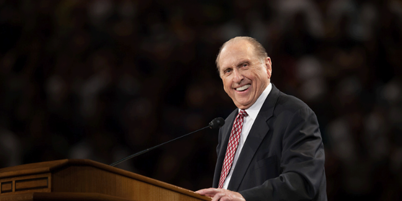 President Thomas S. Monson smiling from the pulpit at a Brigham Young University devotional.