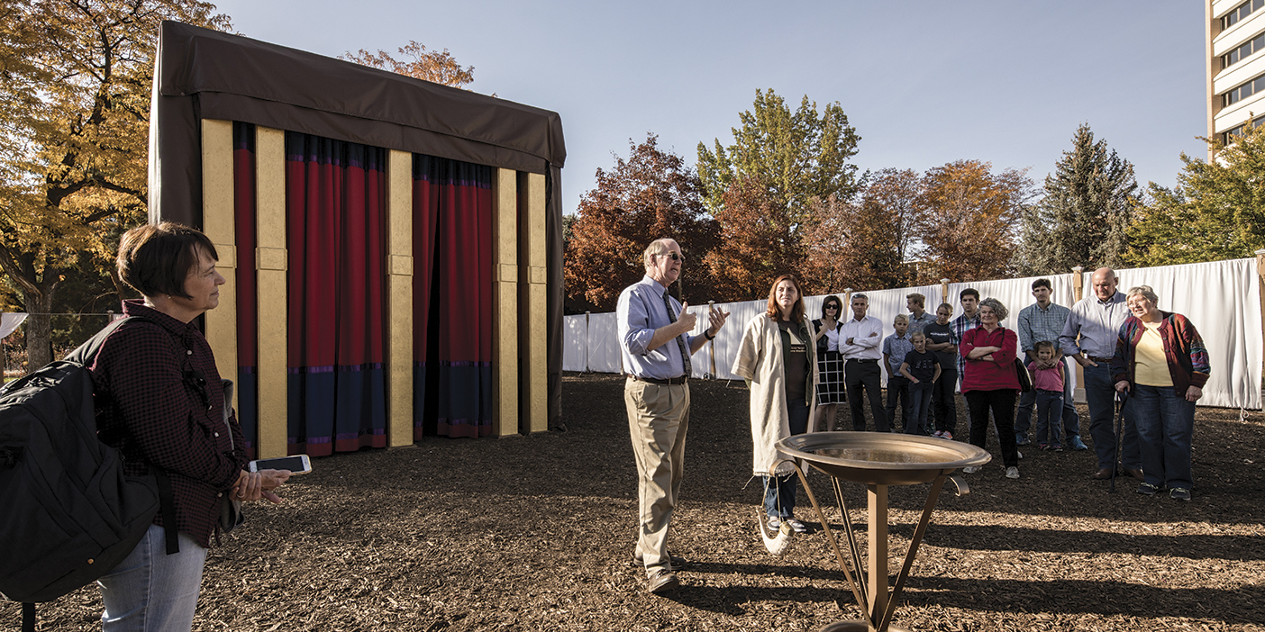 BYU Hebrew professor Donald Parry stands outside a life-size replica of Moses's tabernacle, talking with a small group of visitors.