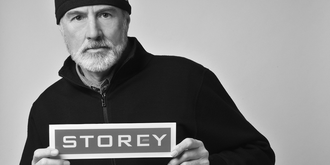 Black and white photo of David Storey, holding up a sign that reads: "Storey."