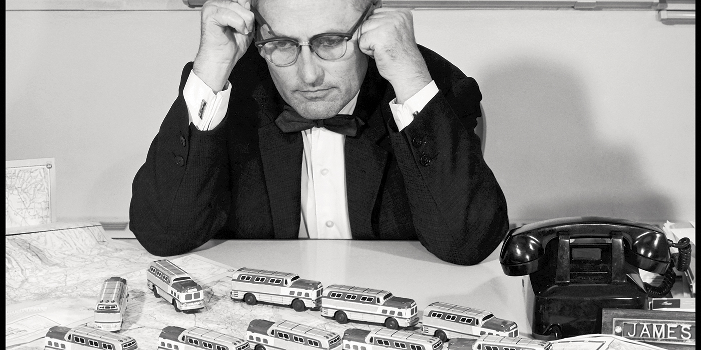 A black and white photo of James Lawrence staring down at a desk with toy busses on a map.