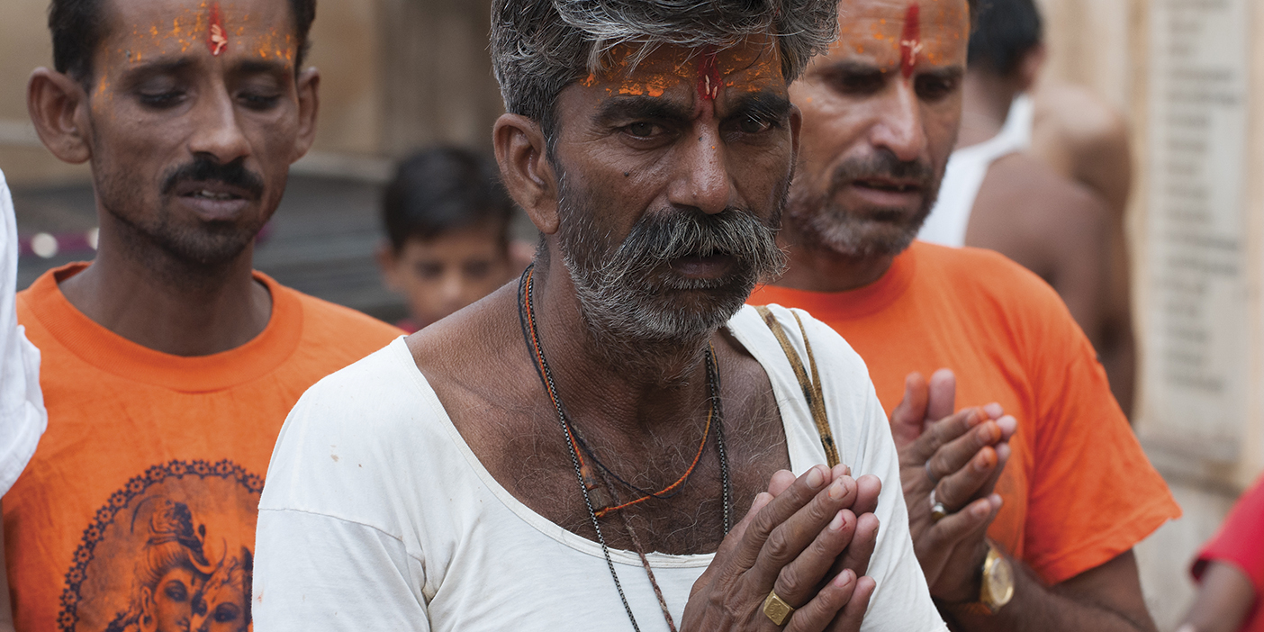 Three Indian men with red paint on their foreheads and their hands clasped in prayer.