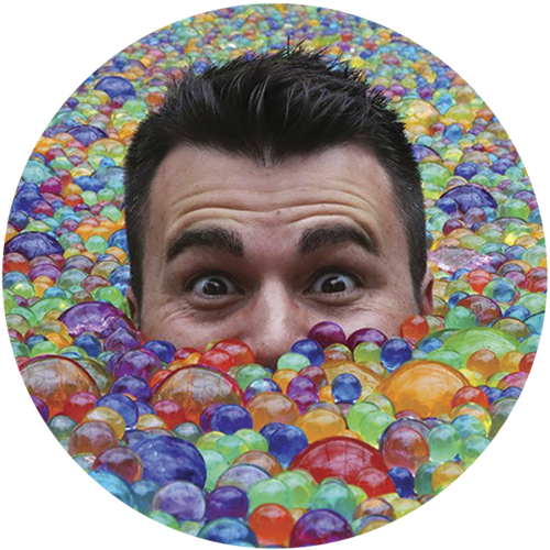 YouTube Mark Rober sitting in a pool full of colorful Orbeez water beads.