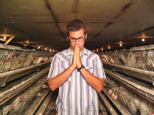 Director Jared Hess stands in the chicken house. He clasps his hands together and holds them to his face as if deep in thought.