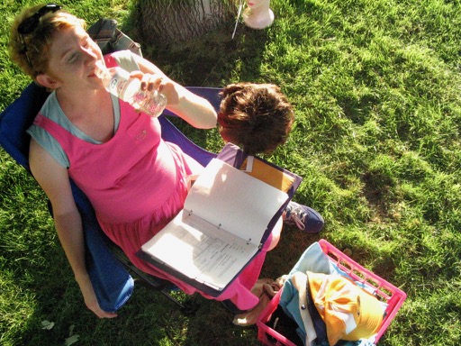 Jerusha Hess drinks water in the summer heat while sitting in a camping chair with Pedro's wig in her lap.