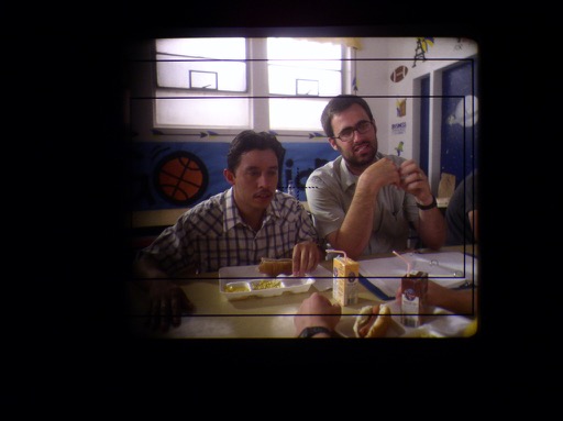 The photo looks through the camera viewfinder to nap a shot of Pedro sitting at the Preston High lunchroom table with director Jared Hess.
