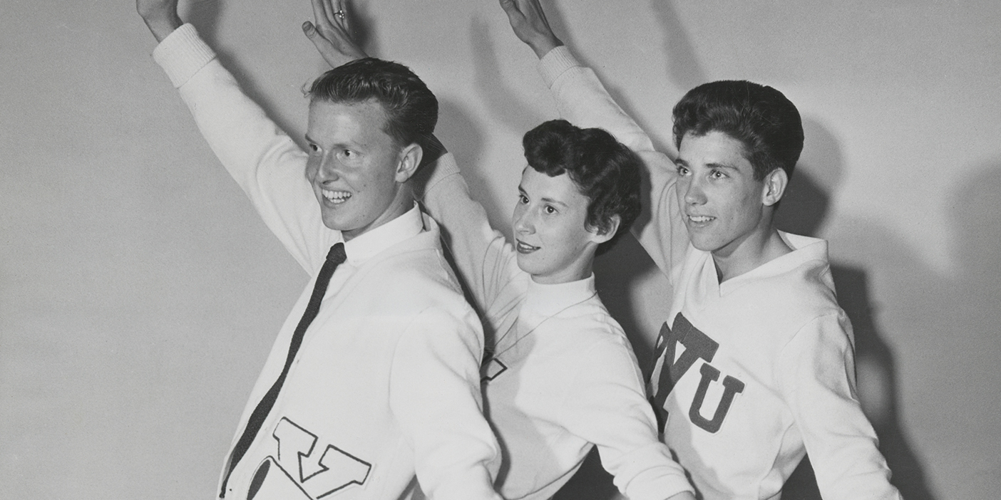 A black and white photo of three cheerleaders from 1954 raising their arms.