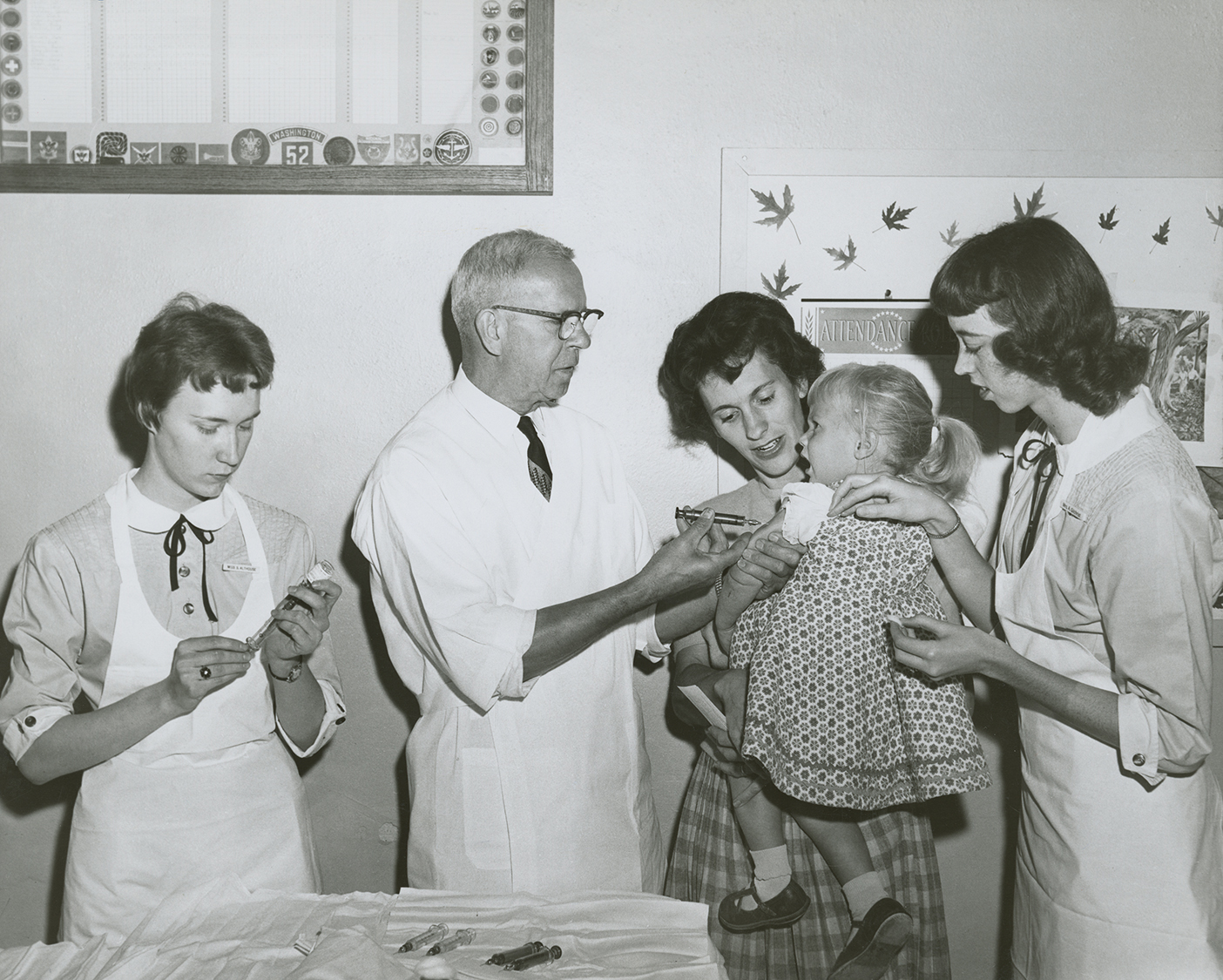 A black and white photo of BYU nursing students helping a doctor give a little girl a shot.