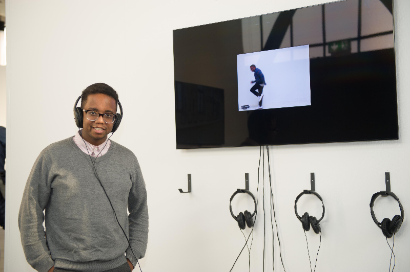 Julian Harper, wearing headphones, standing next to a television screen playing his award-winning video.