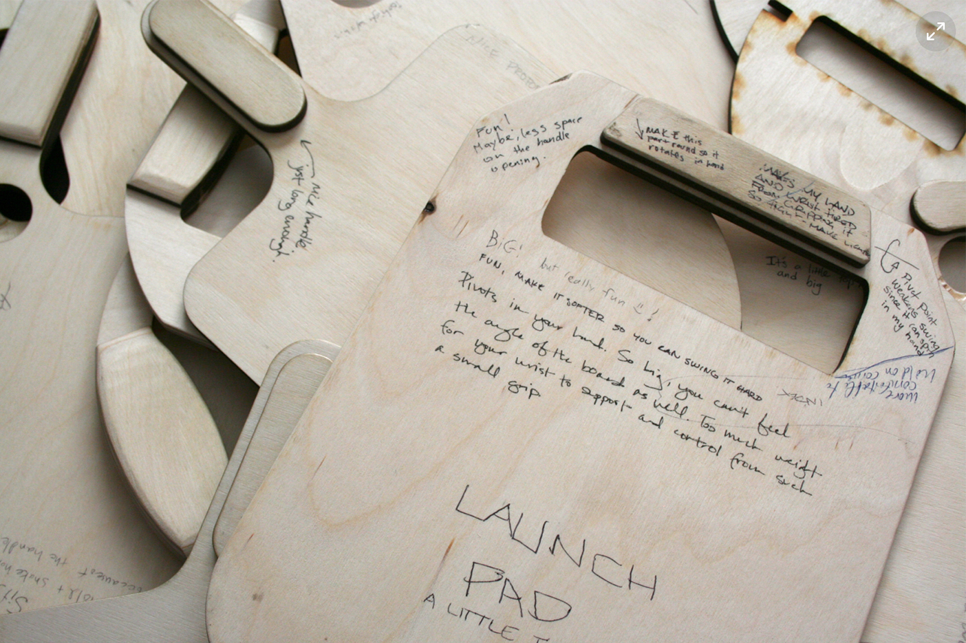 A closeup of plywood paddle iterations with writing scrawled on the paddles.
