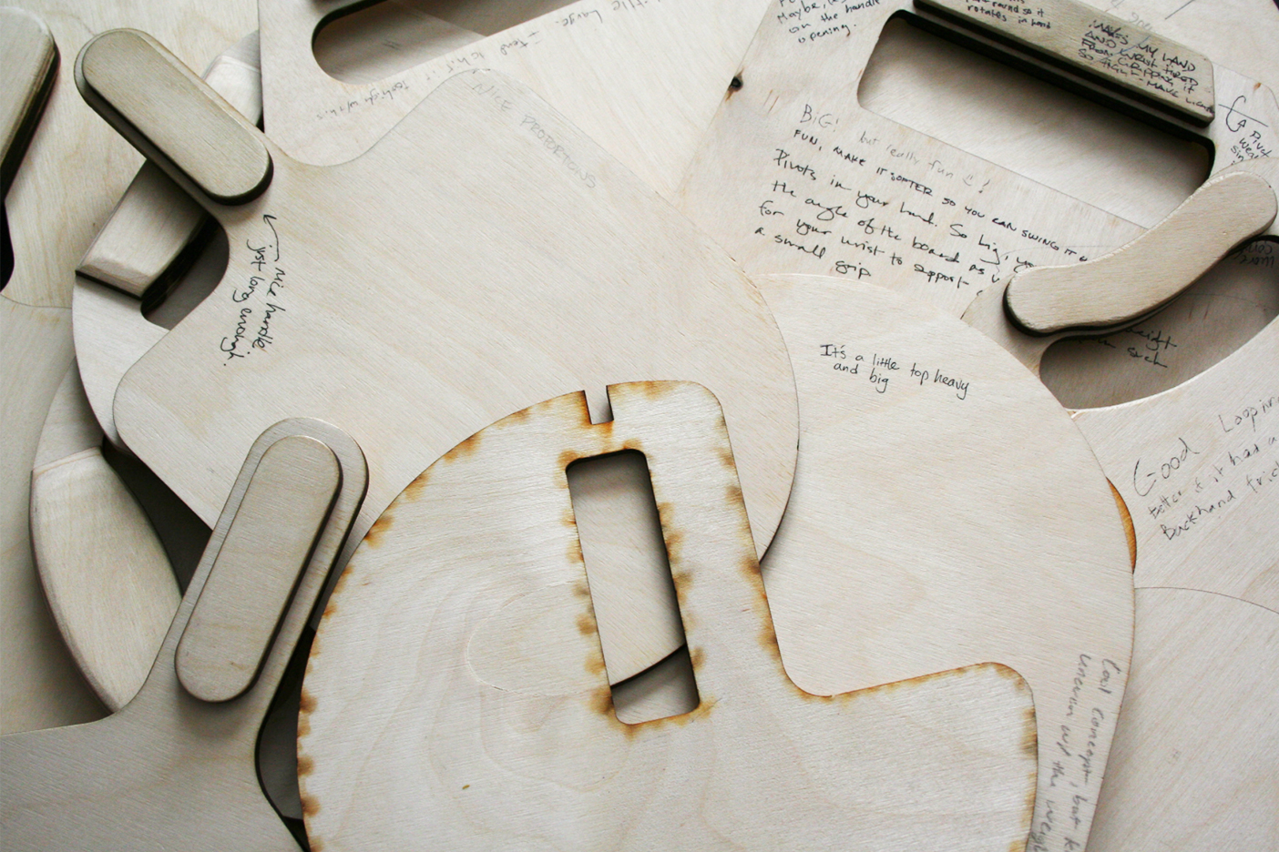 A closeup of plywood paddle iterations with writing scrawled on the paddles.