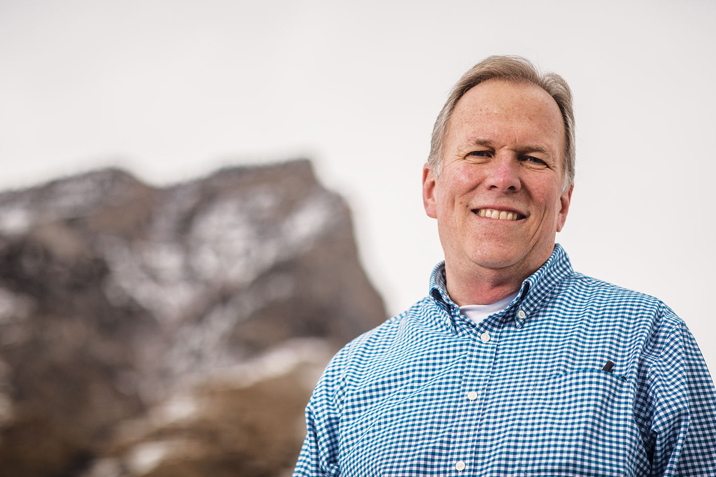 Backed by a mountain peak, BYU grad Joseph Johnston stands and smiles.