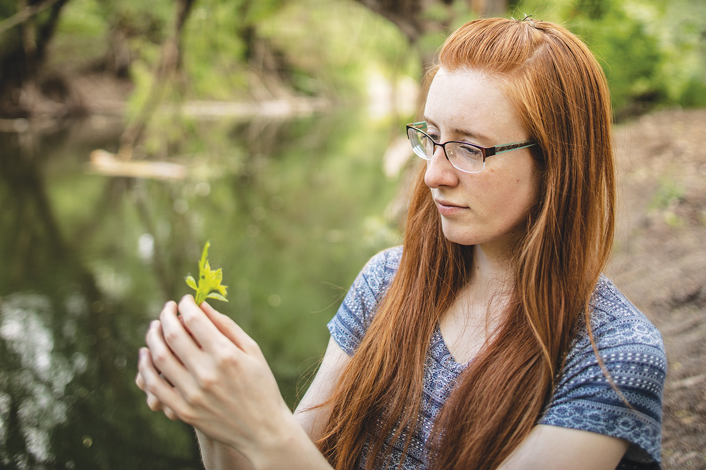 Anne Thomas holding a yellow flower next to a green river