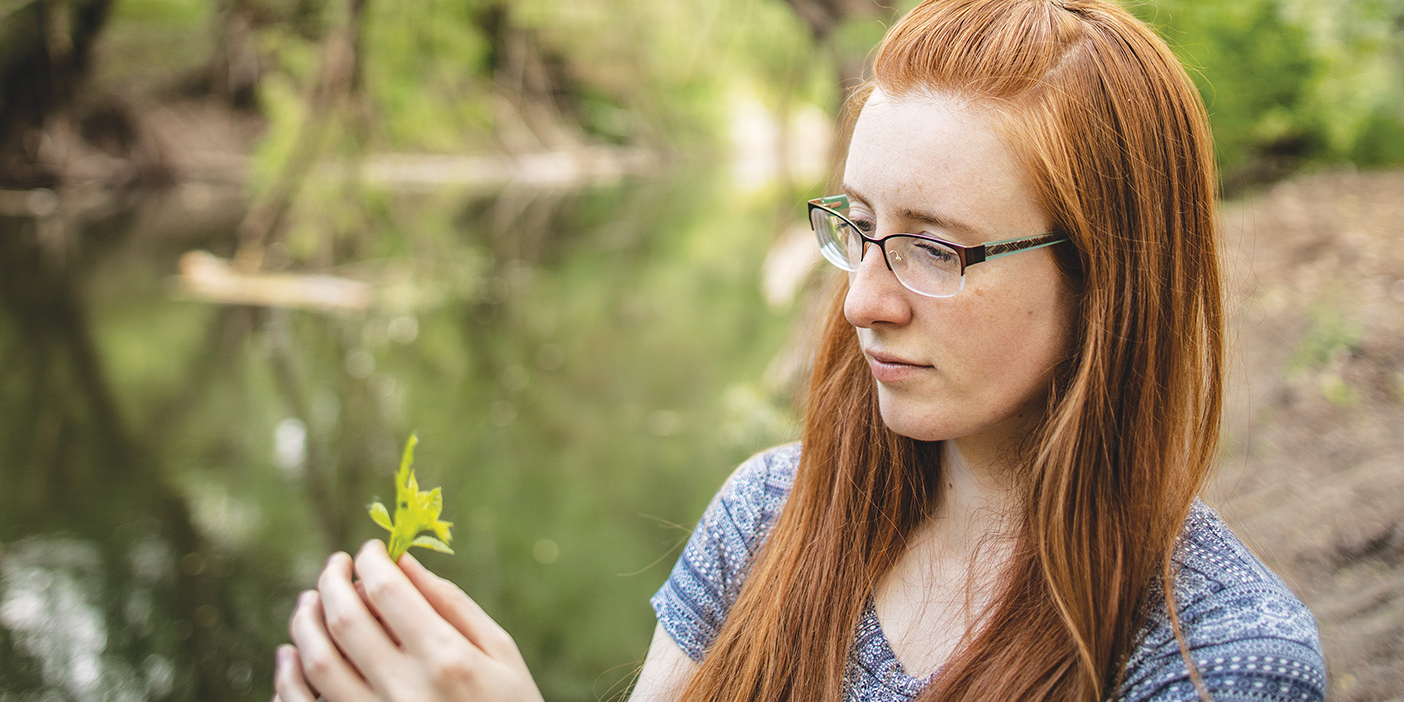 Anne Thomas holding a yellow flower next to a green river