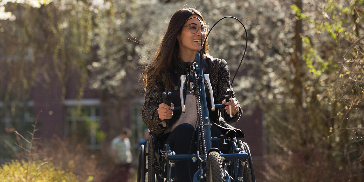 A young woman using a hand-trike wheelchair attachment.