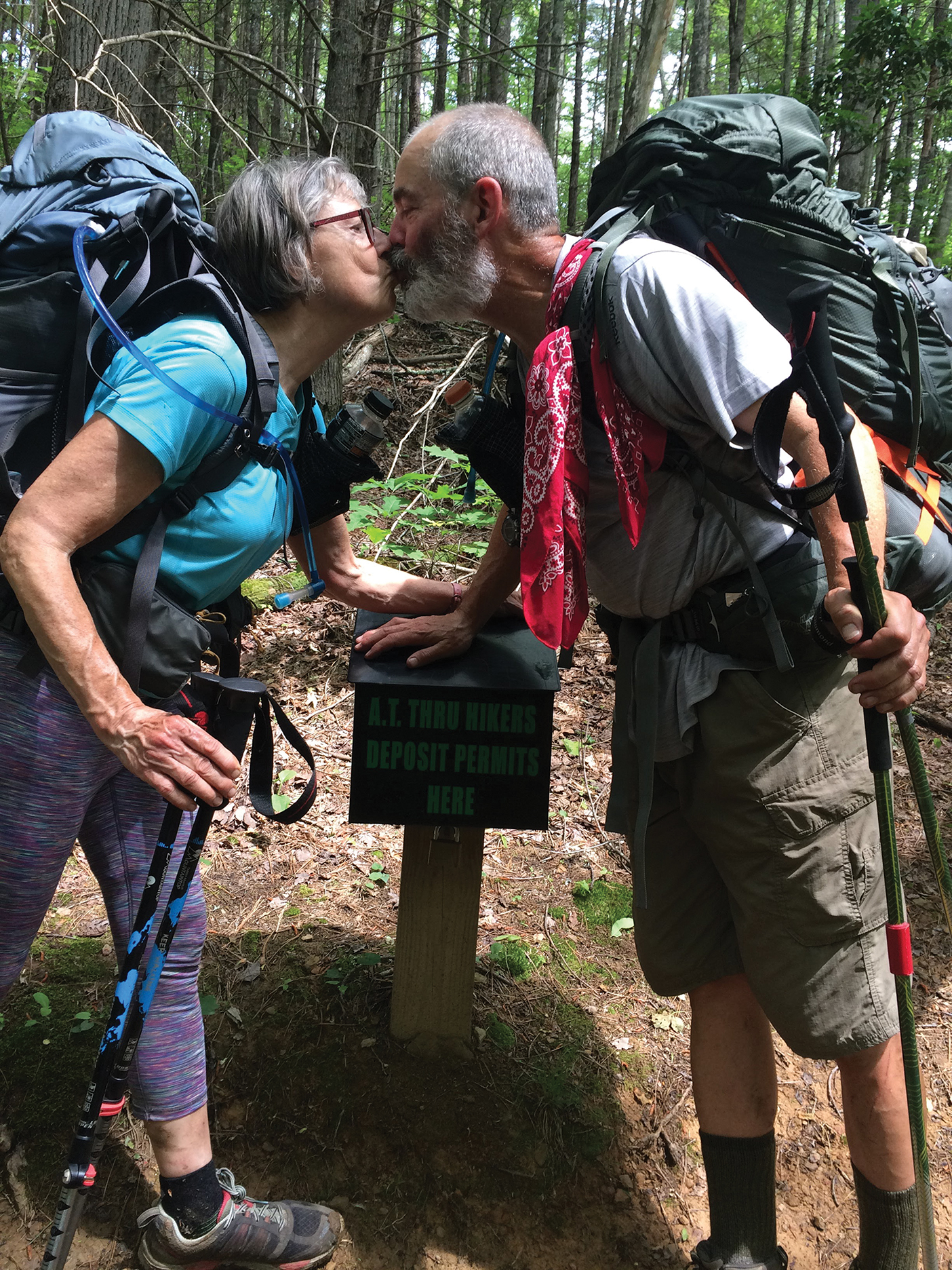 John and Shauna Dickson kiss over a trail sign on the Appalachian Trail