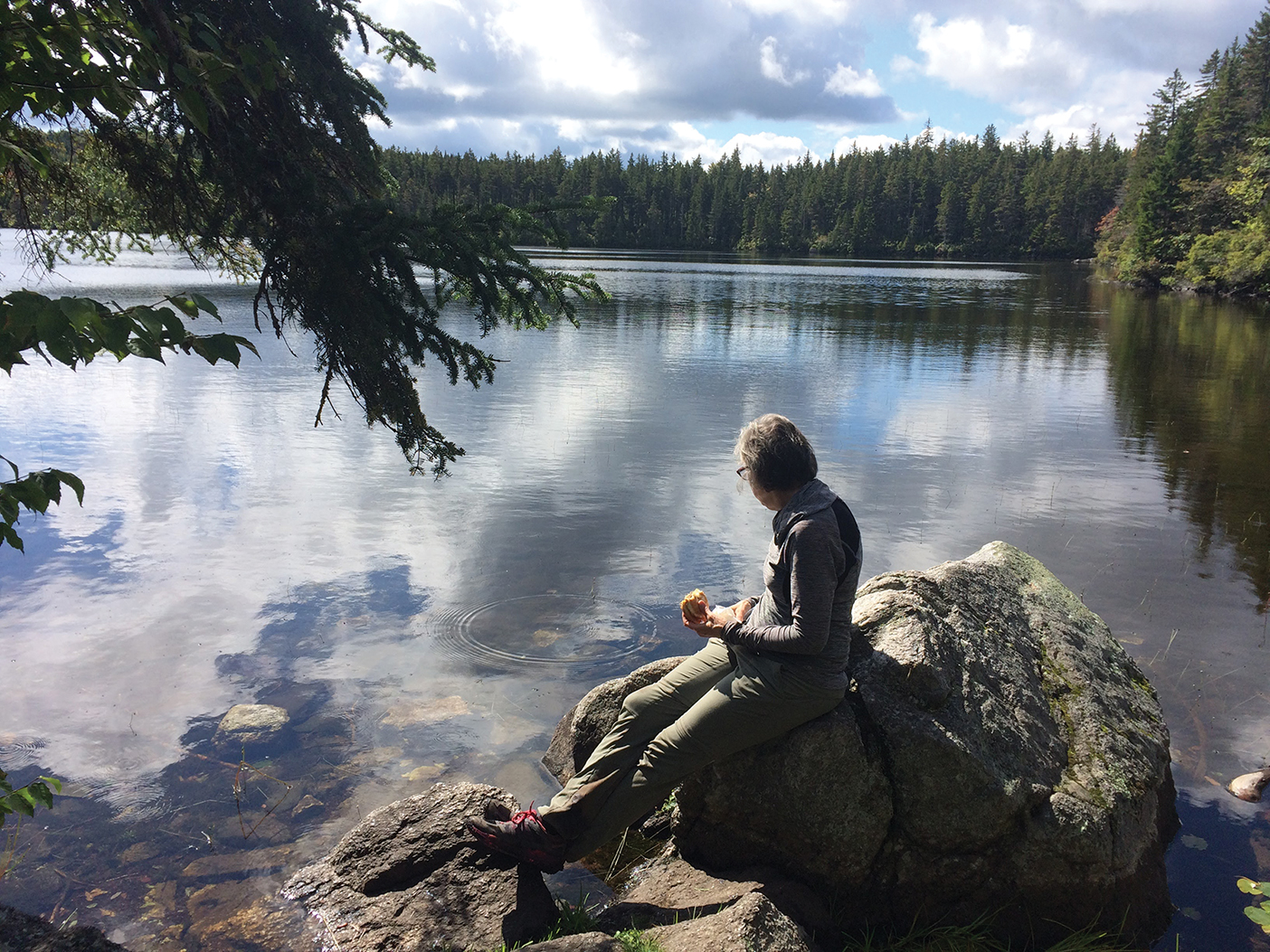 A woman sits on a rock overlooking a lake