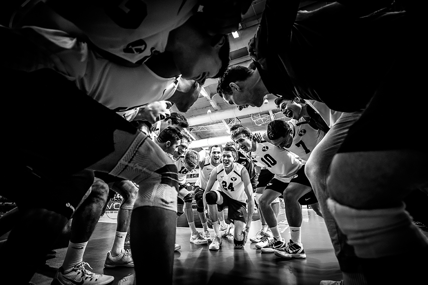 A black and white photo of the men's volleyball team in a huddle.