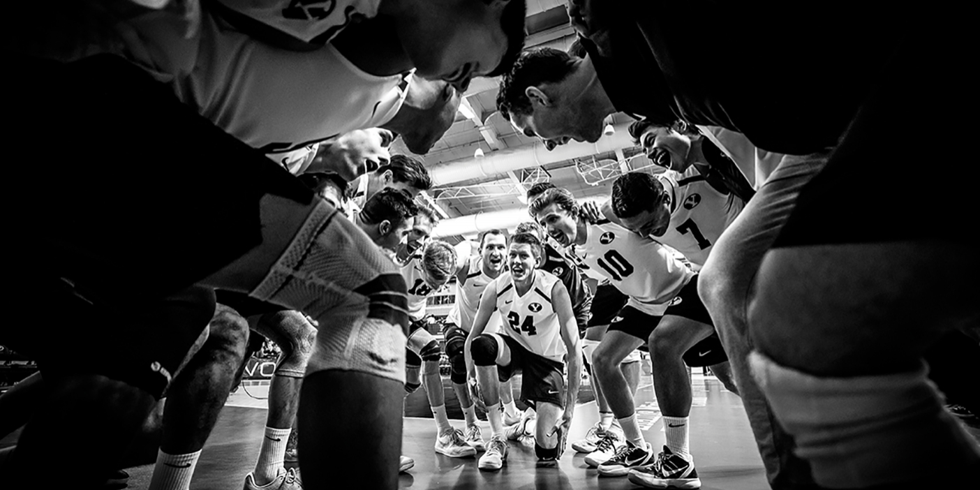 A black and white photo of the men's volleyball team in a huddle.