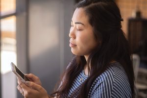 A young woman holding a smartphone launches an app, closes her eyes, and practices breathing exercises.