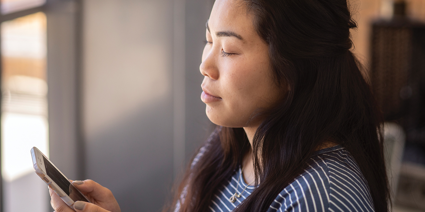 A young woman holding a smartphone launches an app, closes her eyes, and practices breathing exercises.