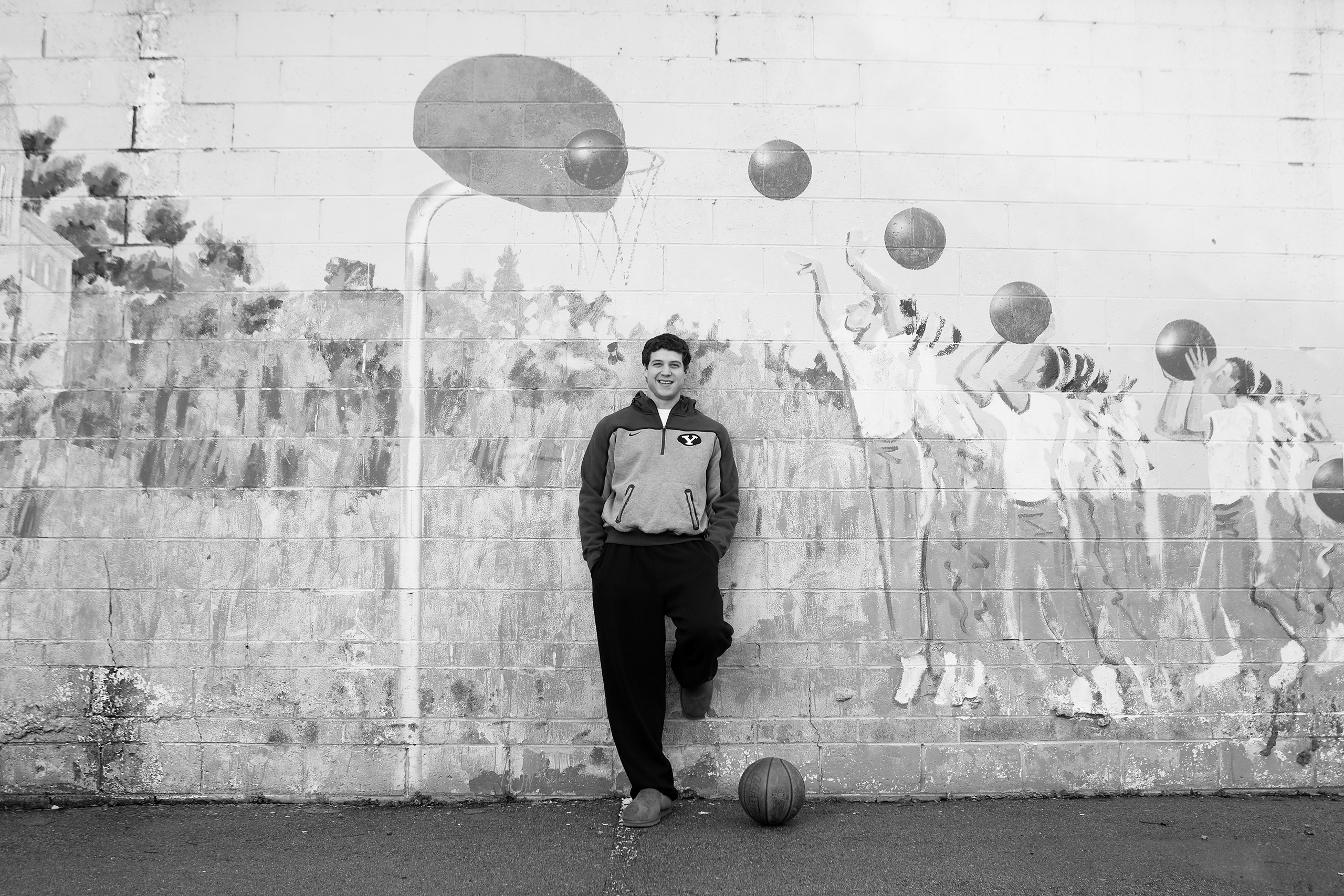 Jimmer Fredette poses in front of a building in south Provo with a mural of several people playing basketball.