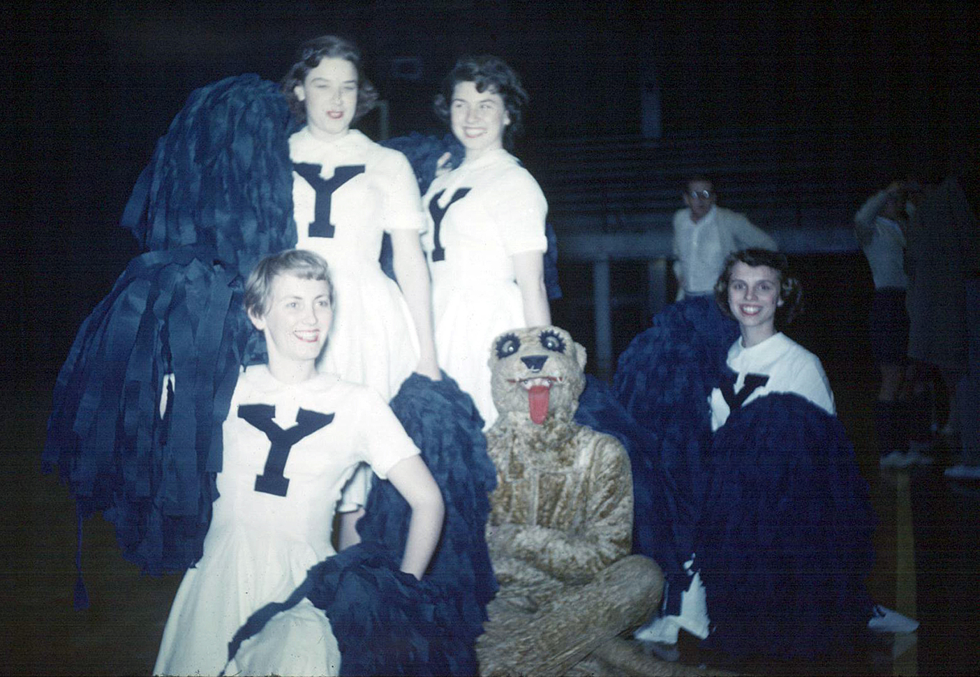 Cosmo poses with three BYU cheerleaders holding pom-poms.