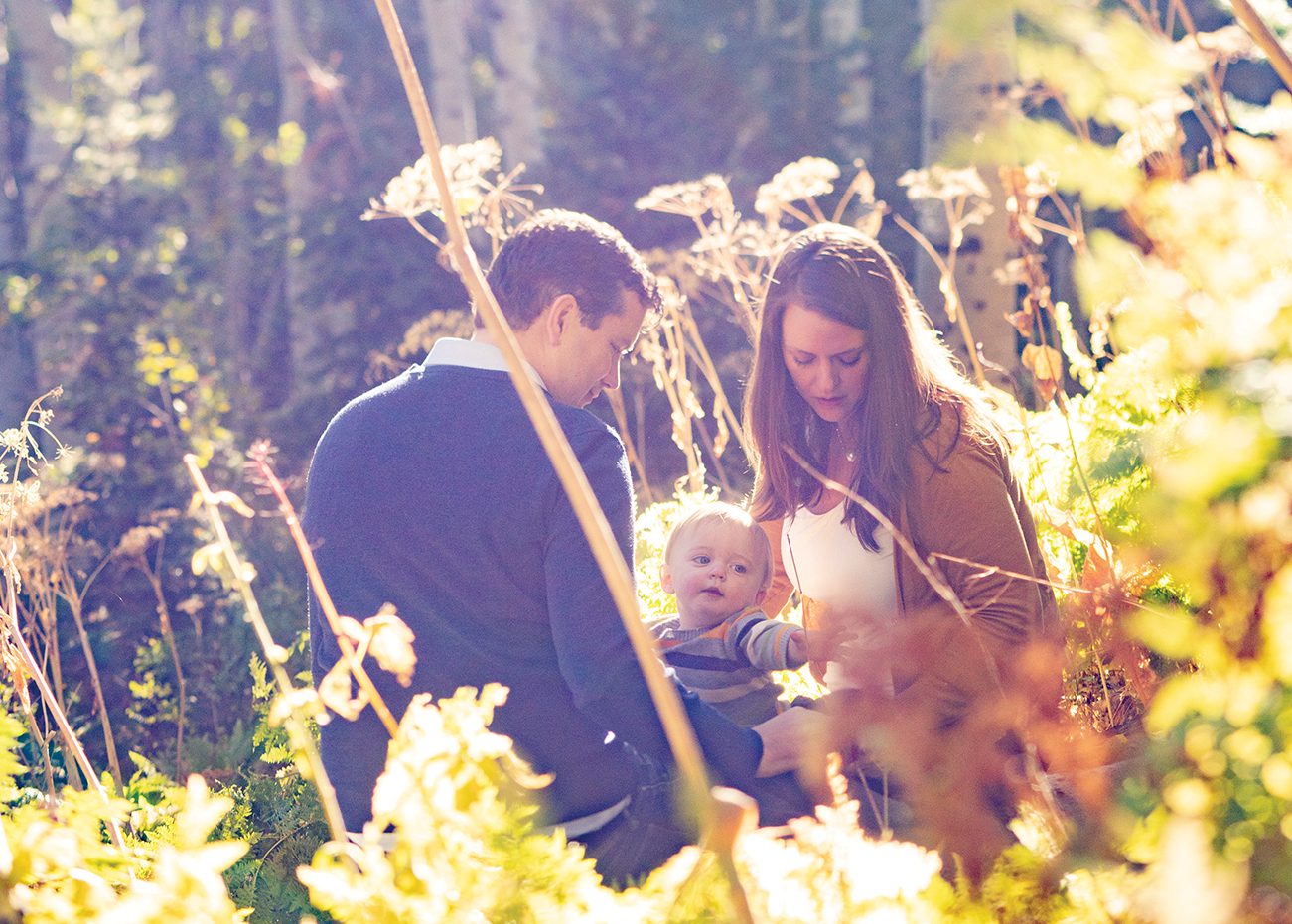 Doug and Ruth Thomas and their son sit in a meadow of fall foliage.