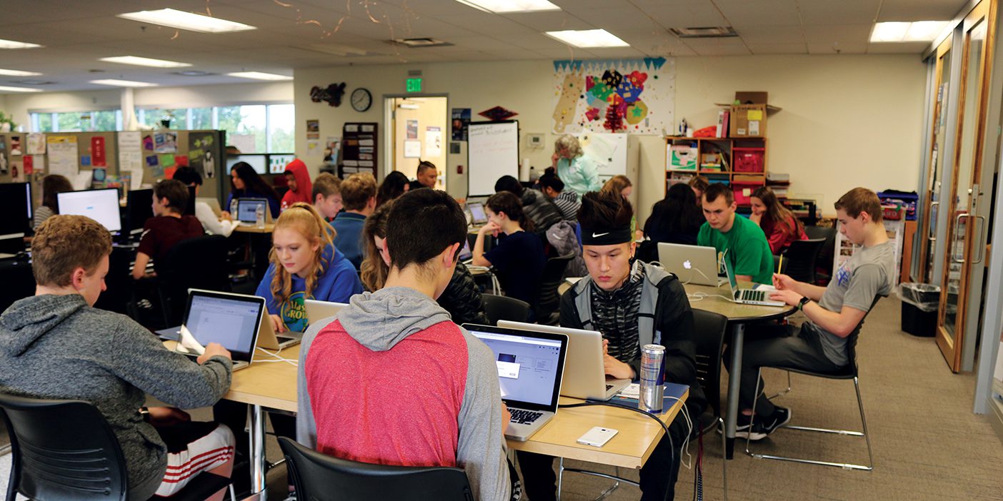 High school students work on college prep coursework on laptops in a classroom.