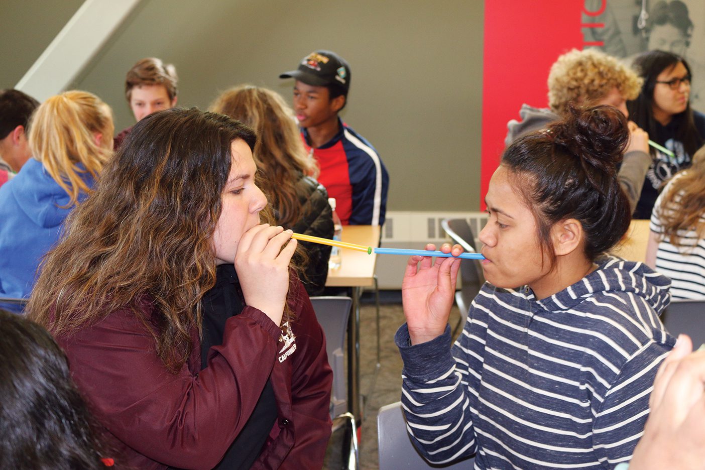 In a get-to-know-you game, two students with straws in their mouths pass a skittle to each other by sucking on straws.