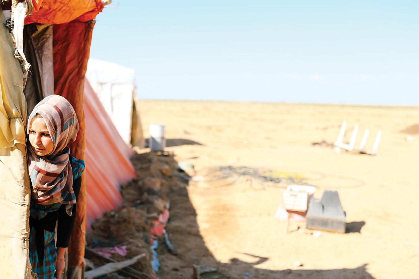 A Syrian refugee woman is looking out from her tent in the Jordanian desert.