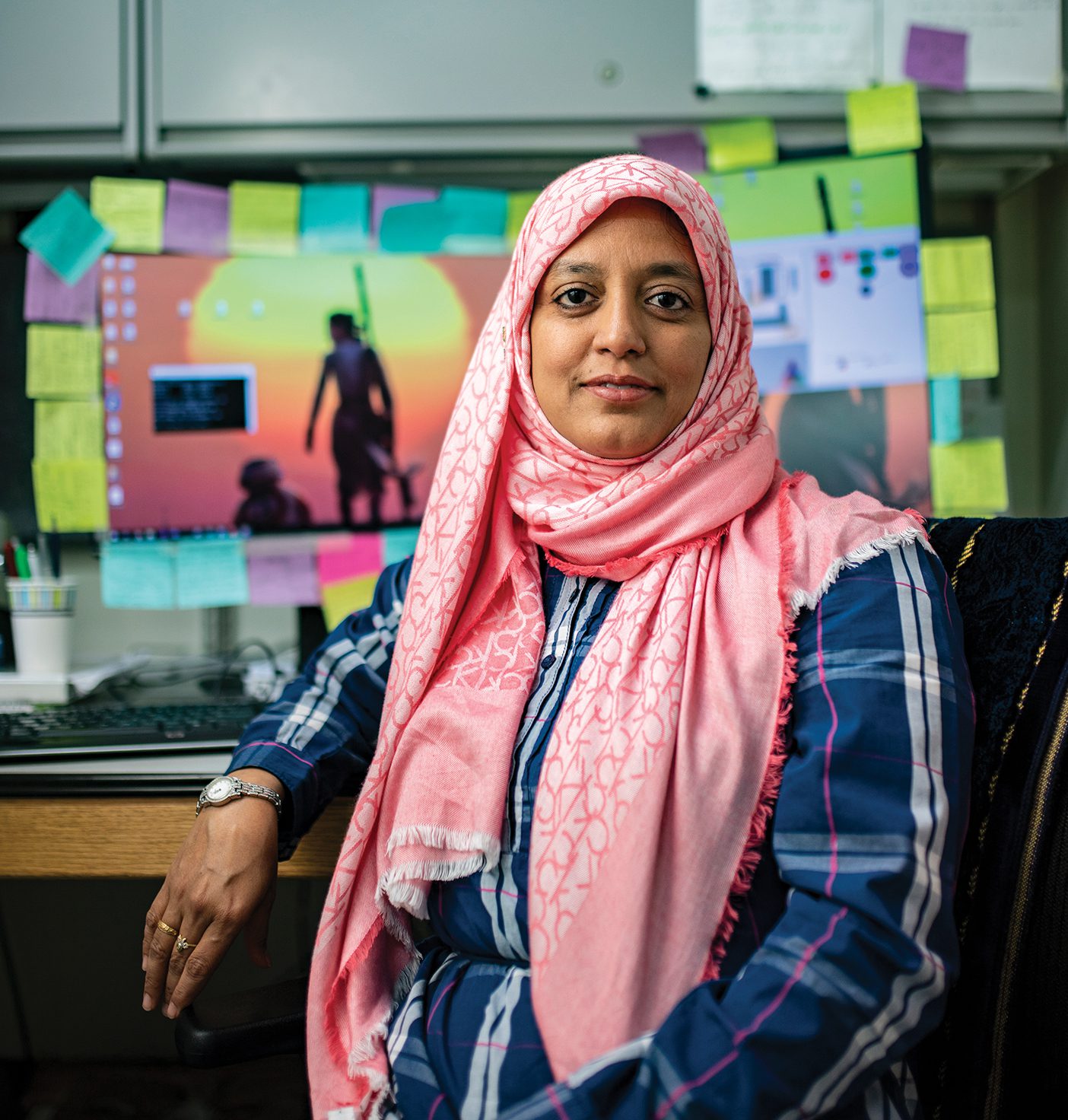 PhD student Meher Shaikh sits in front of her computer, which is ringed with colorful sticky notes.
