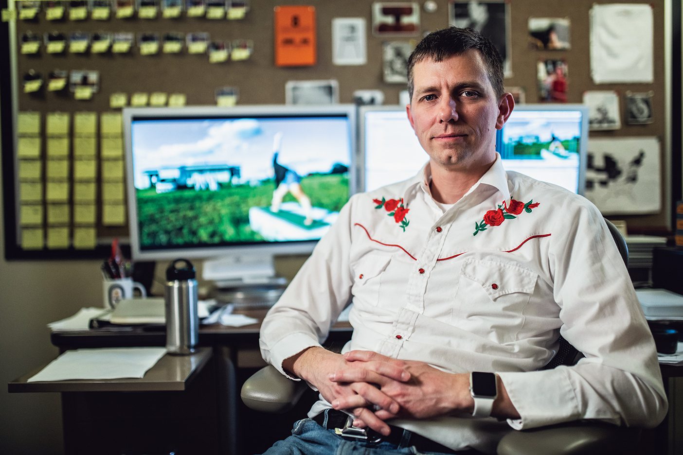 Brad Barber, in an embroidered shirt, sits in his office with footage of States of America on the monitor in the background.
