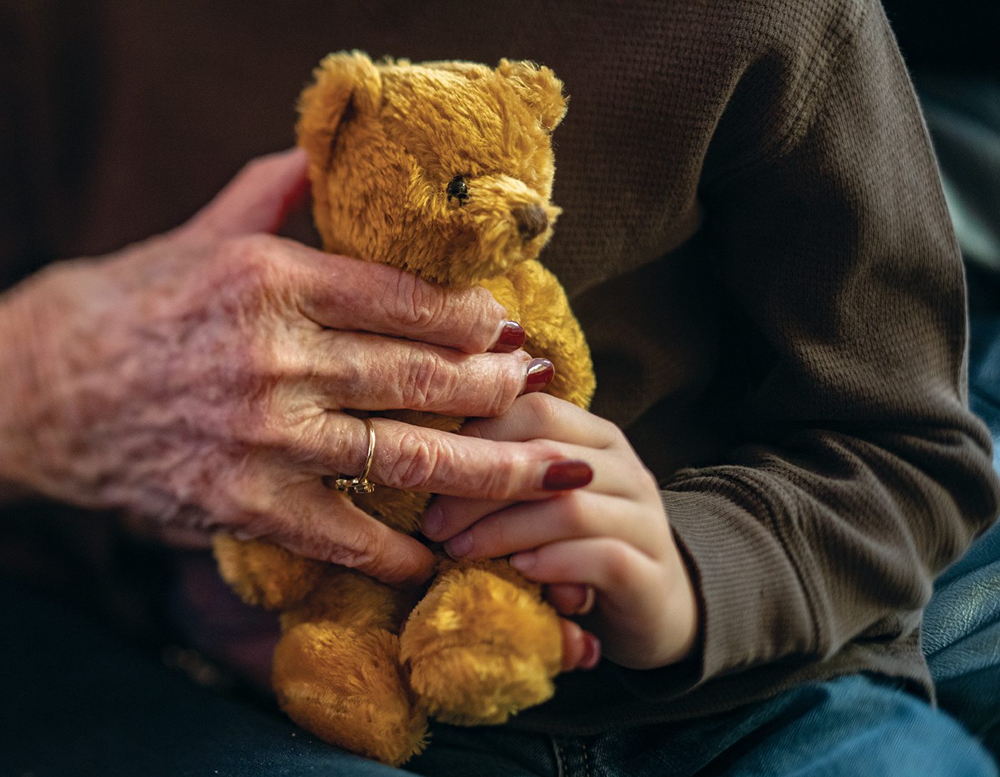 Hands, one young, one old, grasp a golden=brown teddy bear.